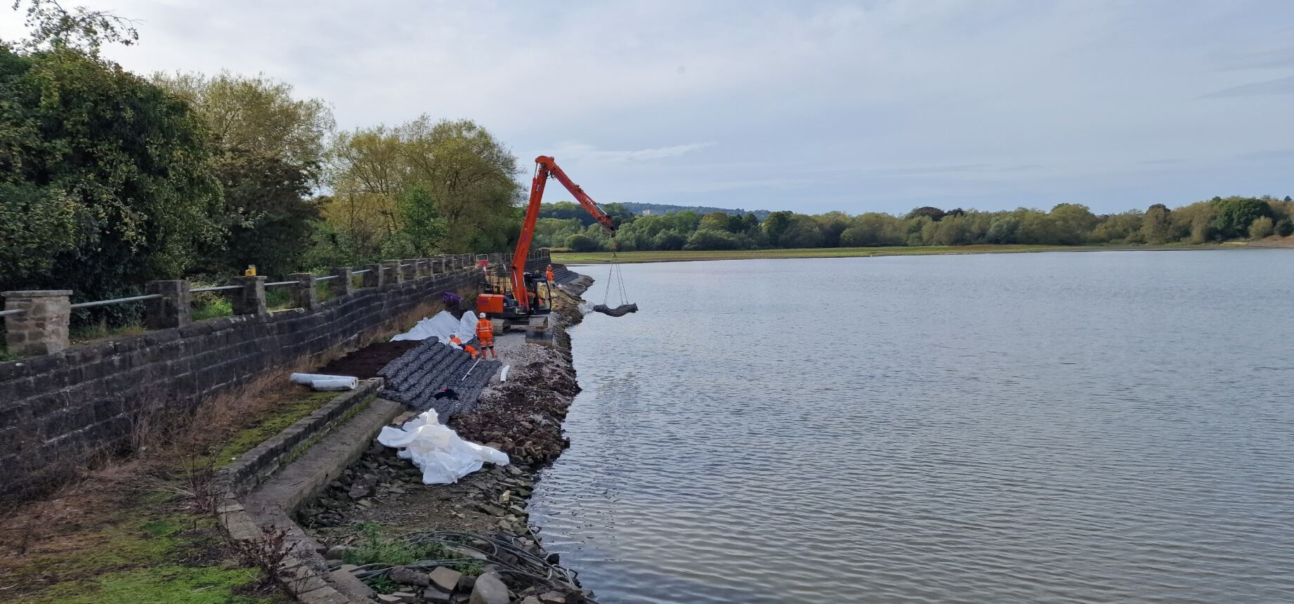large excavator carrying rock backs to install at edge of reservoir